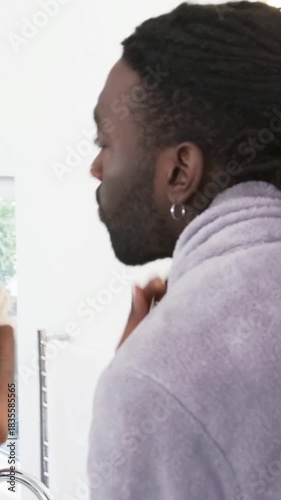 Vertical video: Entering bathroom, man examining jawline in mirror for skin inspection, with towel