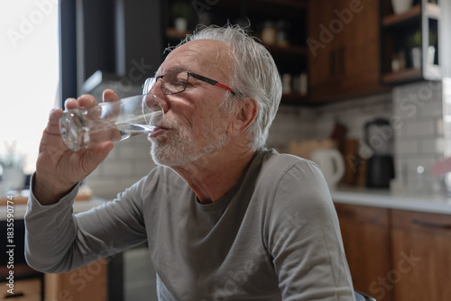 Elderly man drinking a glass of water at home, taking a moment to stay hydrated in a cozy kitchen setting