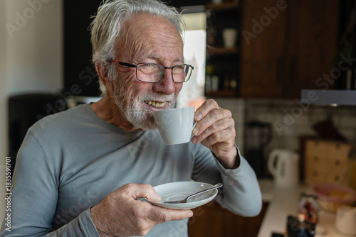 Canvas Print Elderly man sipping hot coffee from a cup while standing in a cozy kitchen, enjo