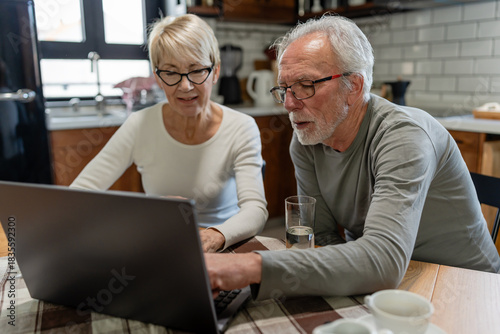 Senior couple using a laptop together at the kitchen table, focused on browsing or managing online tasks