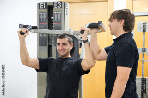 Man exercising shoulders with personal trainer at gym
