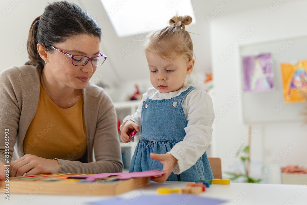 Fototapeta premium Mother and young daughter enjoy a creative crafting activity together, cutting and gluing colorful paper shapes in a bright, cozy home environment