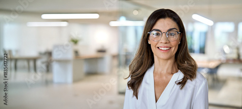 Happy middle aged business woman, smiling 45 years old lady entrepreneur, mature female professional executive manager leader wearing eyeglasses standing in office. Headshot portrait. Banner