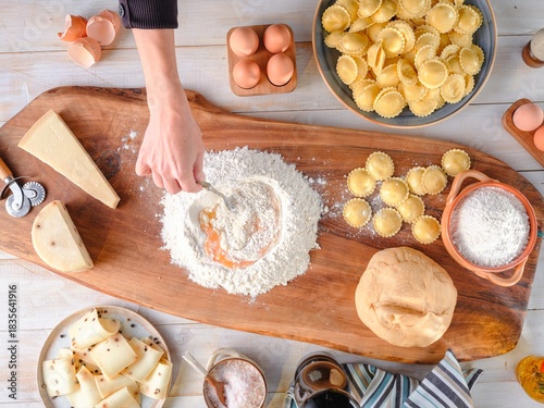 A person is skillfully blending eggs into flour on a wooden board, crafting fresh pasta dough. Dishes of finished girasoli, cheese, and other ingredients surround the workstation