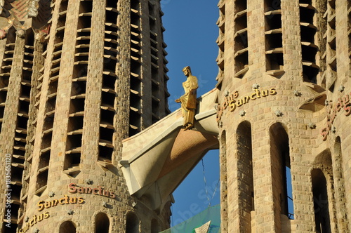 A detailed view of the Nativity Façade’s towers at Sagrada Família, featuring the golden statue and the repeated “Sanctus” inscriptions under warm afternoon light.
