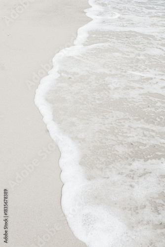 A tranquil coastal scene where smooth sand meets foamy shoreline as gentle waves roll in.Perfect for themes of relaxation, nature, vacation.Demonstrating trendy white color of 2026 year - cloud dancer