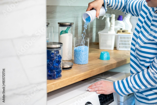 Female housewife hands sprinkle dry blue granular laundry conditioner glass can storage organizing