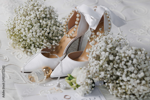Elegant white bridal shoes with flowers and wedding accessories on delicate background