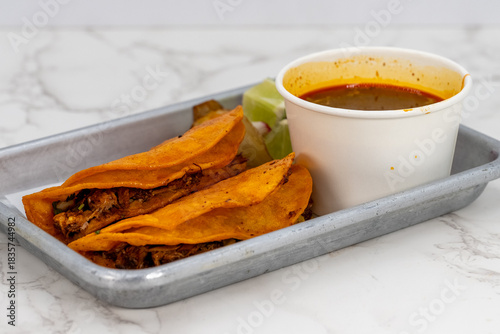 Latino food for a hungry patron includes a pair of birria tacos and consome sauce for dipping