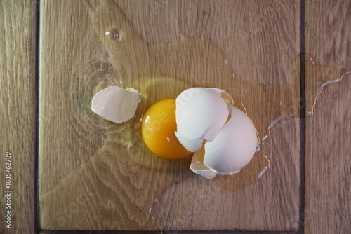 Bilde på lerret cracked raw egg with bright yellow yolk and spilled white lying on wooden surfac