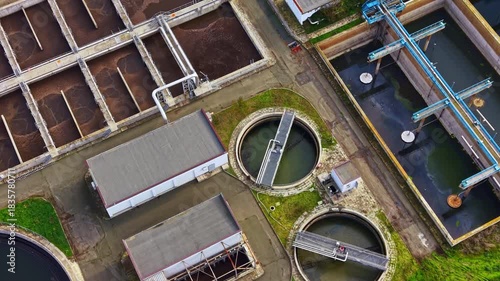 Workers and machines are busy at a wastewater treatment plant, ensuring water is processed efficiently. The complex is surrounded by lush green spaces, showcasing a blend of technology and nature.