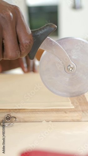 Vertical video: Entering cutter guiding chef's hand in brown top cutting dough for baking on board