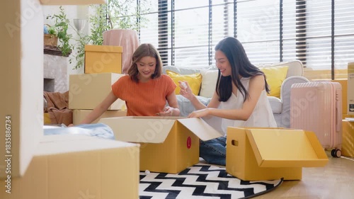 Happy two Asian women friend picking up things out to a paper box while preparing to move in of the new home. Relocation concept