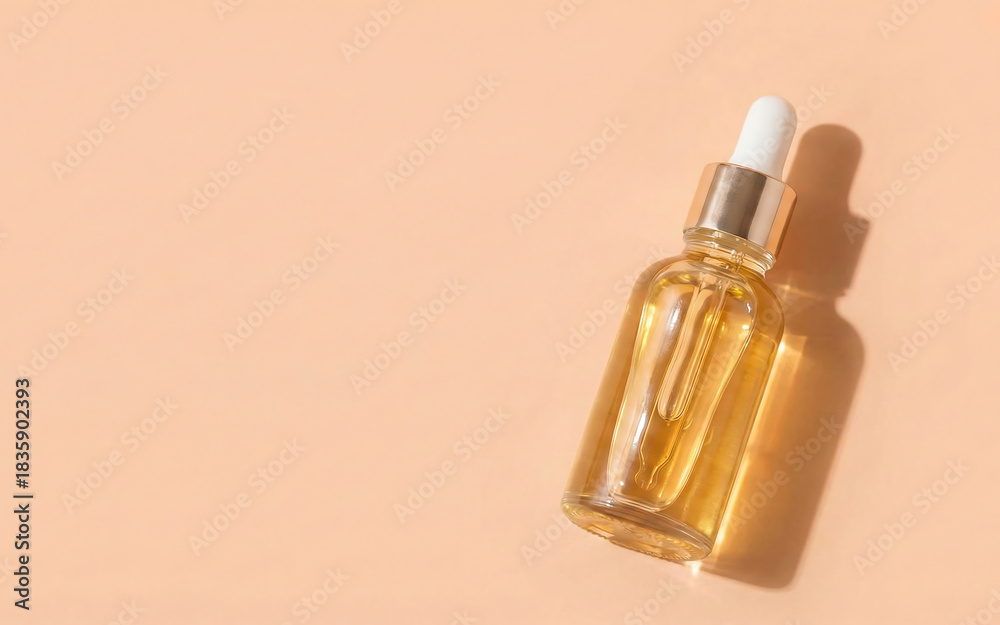 Naklejka premium Close-up of a glass serum bottle with a dropper on a peach background