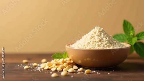Aesthetic presentation of a small bowl brimming with finely textured, pale yellow grain powder beside a scatter of whole grains and a sprig of fresh green leaves