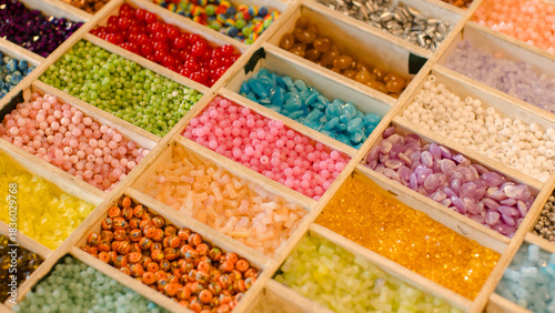 Vibrant collection multicolor craft beads neatly arrange in wooden organizer boxes compartment showcases unique textures hues, handcrafted creating charming slow fashion bracelets inspiring display.