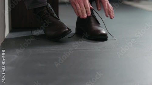 Slow motion dolly shot of young man lace up his brown leather chukka boots indoor