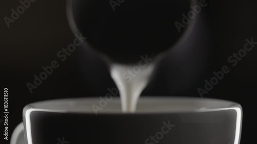 Slow motion pour steamed milk into espresso in white cup closeup