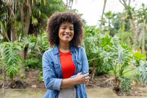 African American woman standing on wooden deck in lush garden surrounded by tropical foliage
