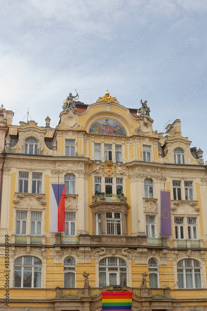 Fototapeta premium ornate yellow facade with pride flag, decorative gables and sculpted balcony framed by vertical national