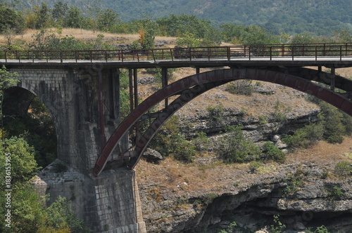 Exploring an old bridge over a canyon surrounded by greenery and rocky formations in a quiet natural setting