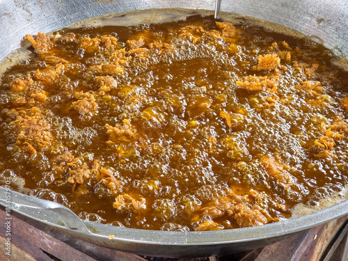 Bubbling hot oil frying fried crispy chicken pieces in a large metal pan with rich golden brown