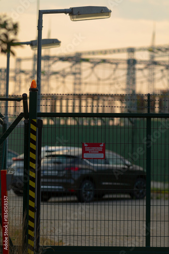A car is currently parked behind a tall fence that clearly displays a no parking sign, indicating that parking is prohibited in this area