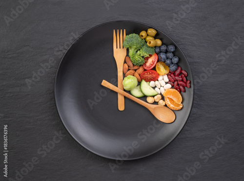 Intermittent fasting concept, spoon and fork on a black plate with food looking like a clock