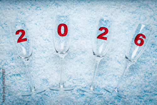 Champagne Glasses with Red 2026 Numbers on Snow Background. New Year celebrations, holiday marketing, greeting cards, event invitations