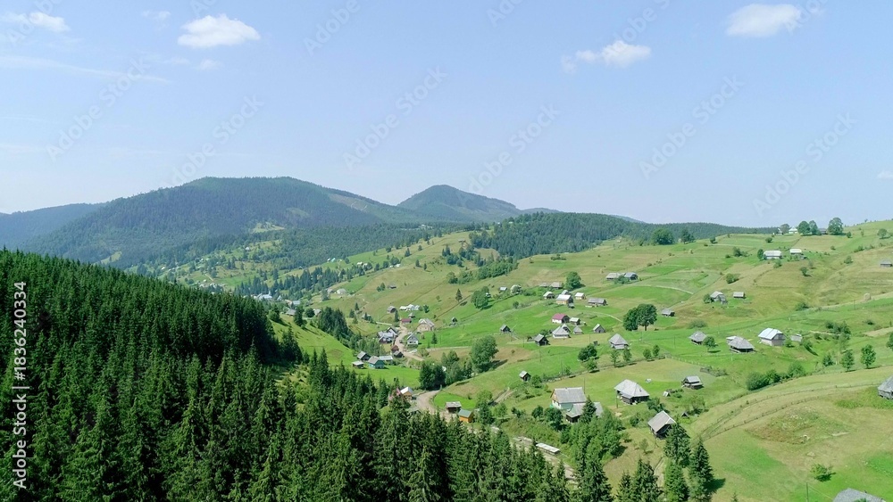 Obraz premium View above green field and village, hills and mountains