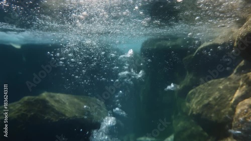 Bubbles rising up from the rocky bottom of deep blue water creating an ethereal underwater background texture