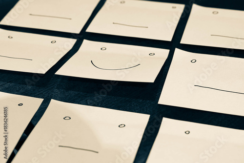 Sticky notes with sad expressions, the middle one is smiling, conceptual positivity image.