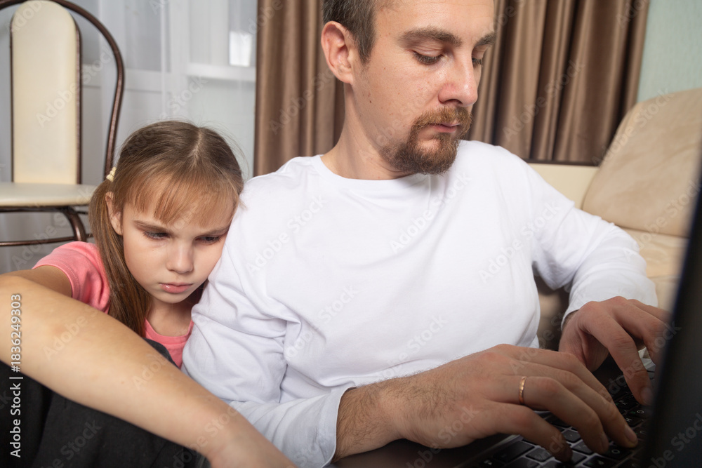 Obraz premium Young focused man working on laptop at home, sad little girl touching his shoulder, want dad to play with her