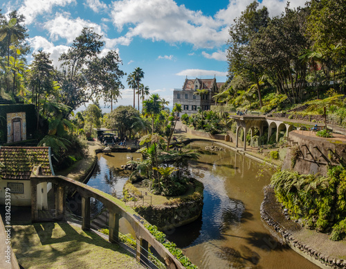 A serene garden scene in Madeira Monte Palace tropical garden in Funchal with lush greenery, a tranquil stream, and traditional architecture in the background. Ideal for nature lovers and tourists.