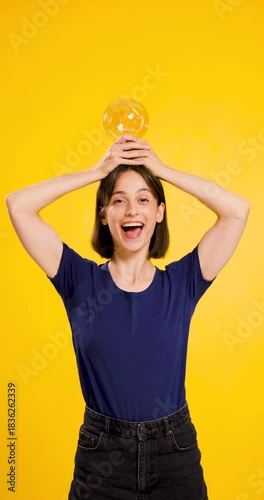 Young woman in blue shirt holding a light bulb over her head against a yellow background