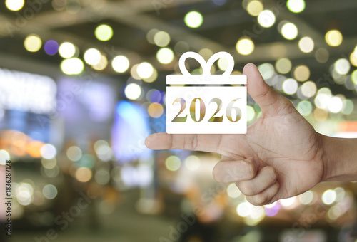 Gift box happy new year 2026 flat icon on finger over blur light and shadow of shopping mall, Business shopping online 2026 concept