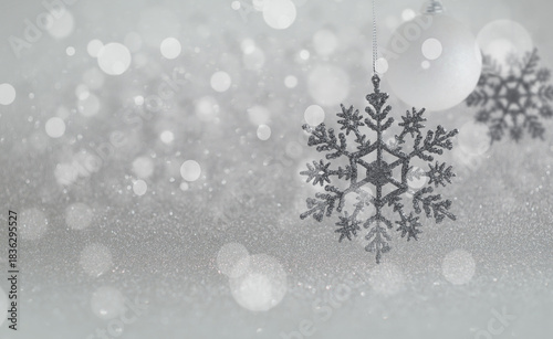 Sparkling Silver Snowflake and White Ornament on Glittering Winter Background. A delicate silver glitter snowflake ornament hanging near a matte white bauble against an ethereal, highly textured backg