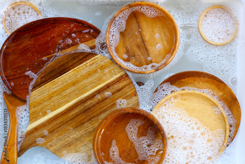 A top-down view of various wooden spoons and bowls soaking in soapy water, ready for a thorough cleaning.
