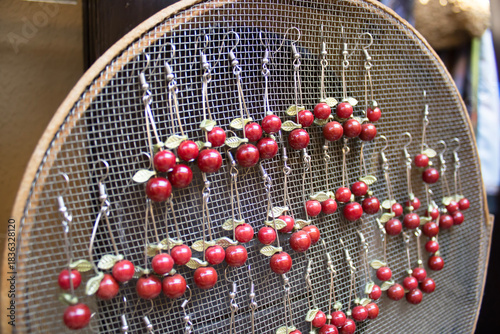 Macro closeup of handmade cherry earrings with glossy ceramic beads and metal leaves on a wire mesh frame, shallow depth and copy space, for fashion detail, product display, craft learning, seasonal g