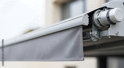 Close-up view of a modern retractable awning mechanism with grey fabric partially extended, showcasing its gears and housing.