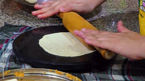 macro shot showing indian snack samosa being rolled with a rolling pin on a marble top and cut for the preparation of the cones