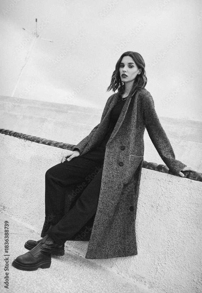 Naklejka premium Street fashion: attractive girl dressed in long gray coat. Outdoor portrait of cute young woman. Black and white