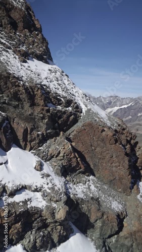 Side of a rocky alpine mountain covered in snow with other mountains visible in the background Switzerland