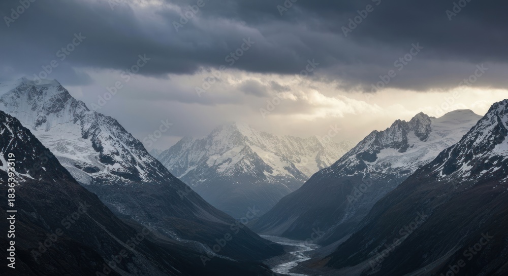 Fototapeta premium Jagged snow-capped peaks under a dramatic, overcast sky, valley below