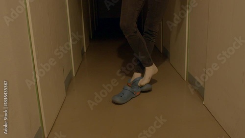 Person performs stable stepping exercises in corridor wearing slippers deliberately, Patient engages in cautious balance training while walking in hallway with slippers and careful foot placement