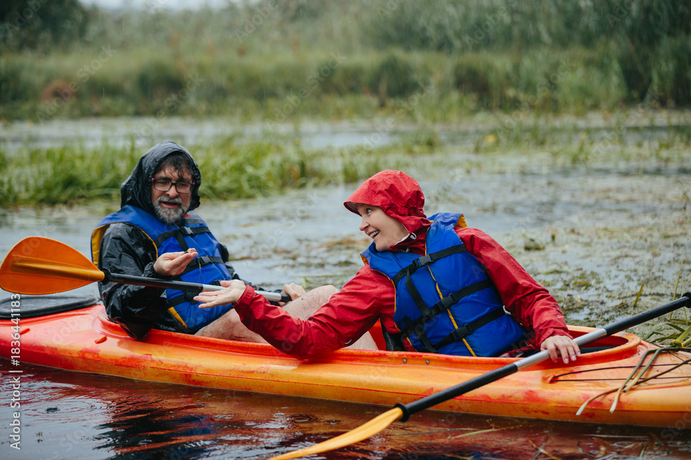 Obraz premium Senior couple enjoying kayaking adventure during rain