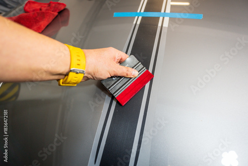 Hand of a specialist installing decals. Application of a black foil sticker on the hood of a sports car. Decal installation.