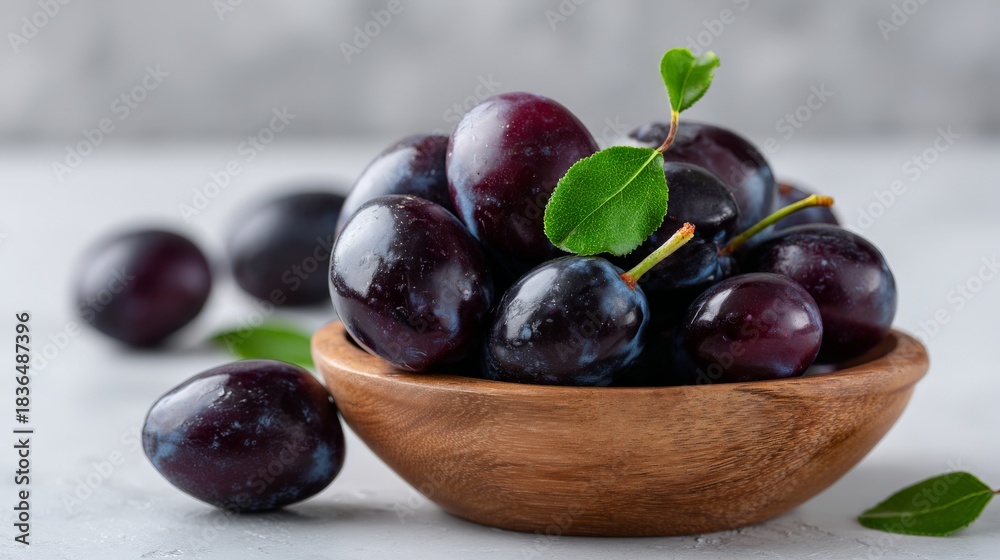Fototapeta premium Fresh juicy plums in wooden bowl with leaves on light background