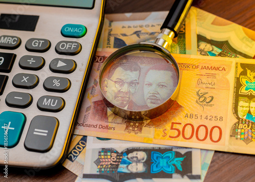 Foto A magnifying glass focuses on a $5,000 Jamaican banknote alongside a $2,000 bill and a calculator