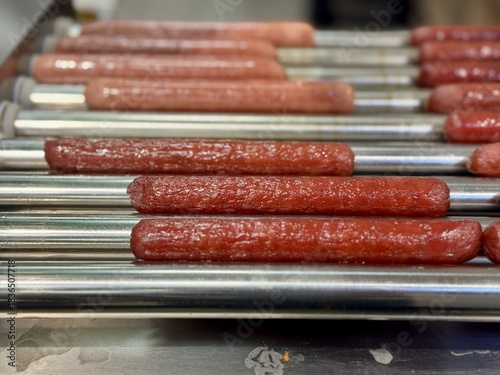 Long delicious hot dogs are sizzling on a roller grill in supermarket indoor, making them the perfect choice for outdoor gatherings and events. Close-up